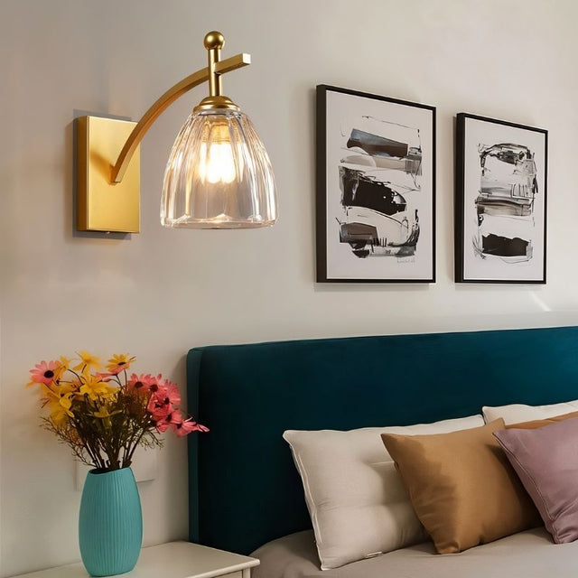 "A gold wall lamp with fluted glass shade in a bedroom setting."