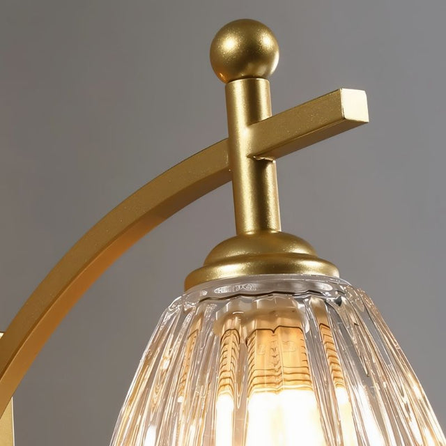 "A close-up detail of the gold wall lamp's iron arm and fluted glass shade."