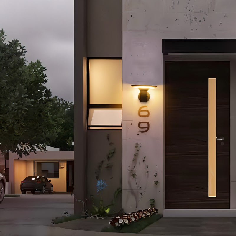 "A modern, cylindrical Luminturs 6W LED outdoor wall light mounted on a textured wall next to a dark wooden door."