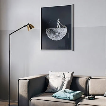 "A modern floor lamp with a black adjustable arm and gold shade, positioned next to a sofa and beneath a framed art print in a contemporary living room."