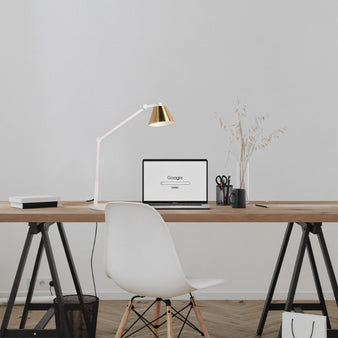 "A modern table lamp with a white adjustable arm and gold shade, illuminating a contemporary home office desk with a laptop and minimalist decor."