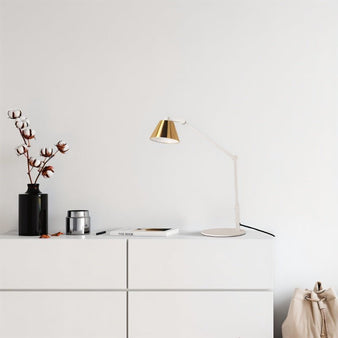 "A modern white and gold table lamp with an adjustable arm, placed on a white sideboard in a minimalist room."