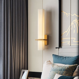 "Elegant wall lamp with alabaster shade and brass accents, glowing warmly in a modern bedroom setting."