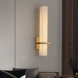 "Modern wall lamp with an alabaster cylindrical shade and brass accents, mounted in a bedroom, providing soft ambient lighting"