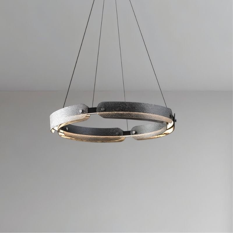 "A modern, circular chandelier with a segmented ring design and textured pattern, made of iron and glass, suspended by thin cables in a room setting."