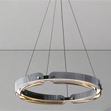 "A close-up view of a modern, circular chandelier with a segmented ring design, made of iron and glass, suspended by thin cables."