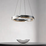 "A modern, circular chandelier with a segmented ring design and textured pattern, made of iron and glass, suspended by thin cables above a dining table."