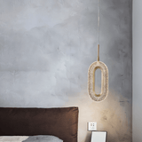 Single Luxin Pendant Light with sculptural oval LED design, hanging beside a brown bed in a minimalist bedroom with textured wall.