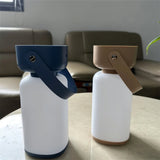 "Two cylindrical table lamps with handles, one in blue and white, the other in beige and white, sitting on a table."