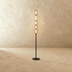 Gold floor lamp with stacked frosted glass shades next to cream sculptural chair in modern studio setting