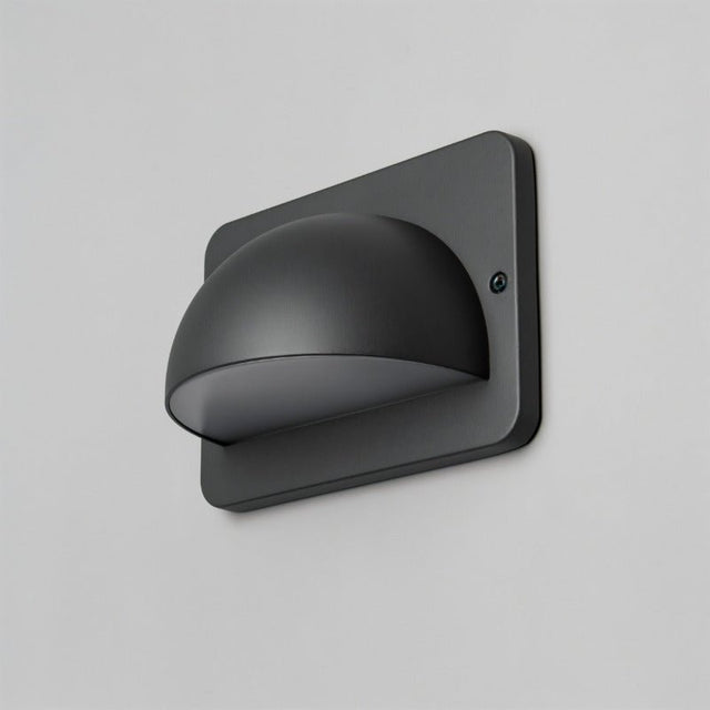 "A modern, dome-shaped outdoor wall lamp with a square base and PC diffuser, mounted on a light gray wall."