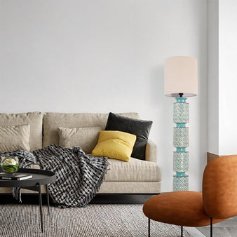 "Floor lamp with a stacked ceramic base in aqua blue and orange geometric patterns, paired with a neutral fabric shade, placed next to a beige sofa in a living room."