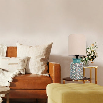 "Table lamp with a patterned ceramic base in aqua blue and orange, paired with a neutral fabric shade, placed on a side table next to a brown leather sofa."