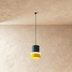 Three modern pendant lamps with stacked cylindrical shades in yellow, pink, and mint green hang against a neutral studio back
