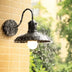 Black metal wall lamp with curved arm mounted on brick wall, actively dripping water in rain.
