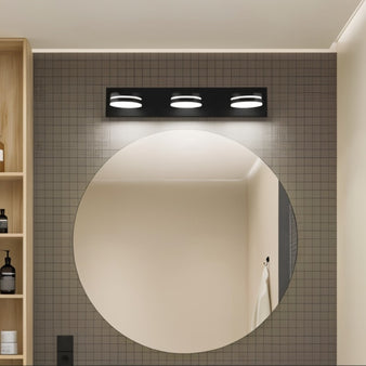 "Black Martil wall lamp with three circular lights above a round bathroom mirror."