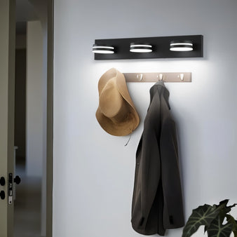  "Black Martil wall lamp with three circular lights above a coat rack in a hallway."