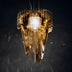 Gold and white cascading pendant chandelier with layered metal strips suspended against a dark background.