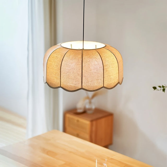 "Mashi pendant light with a fabric shade hanging above a wooden dining table, with a cabinet in the background."