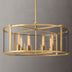 Round brass chandelier with glass panels and vintage-style Edison bulbs against a neutral gray background.