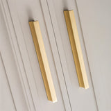 "Close-up of sleek geometric brushed brass pull bars on modern gray cabinets."