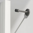 "Sleek, cylindrical door stop in brushed nickel zinc-alloy with extended arm, wall-mounted to prevent a door from hitting the wall in a modern interior."