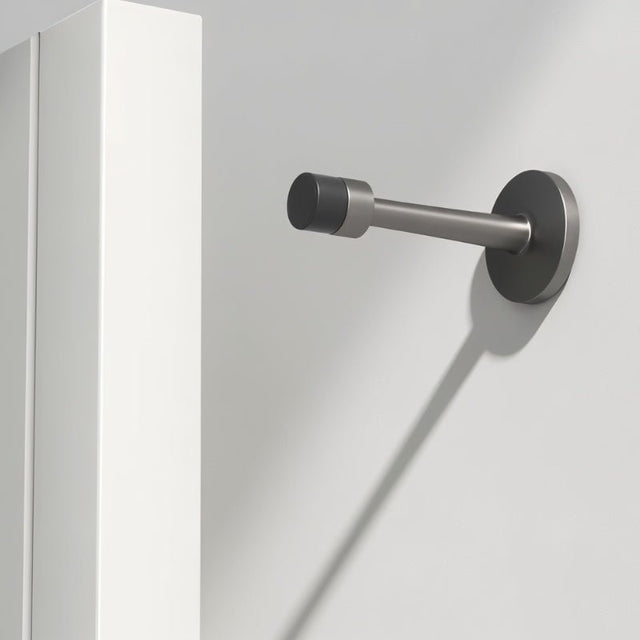 "Sleek, cylindrical door stop in brushed nickel zinc-alloy with extended arm, wall-mounted to prevent a door from hitting the wall in a modern interior."