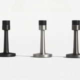 "Collection of sleek, cylindrical zinc-alloy door stops with sturdy bases and extended arms in various modern finishes, designed to prevent doors from hitting walls."