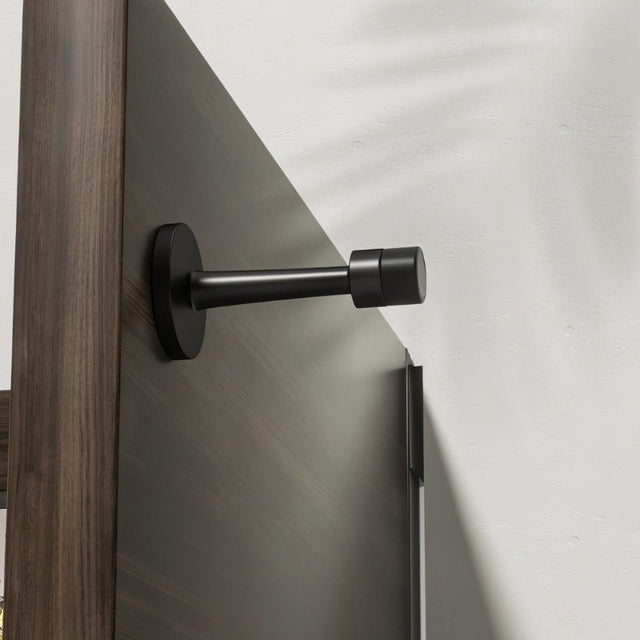 "Sleek, cylindrical matte black door stop with extended arm, wall-mounted to prevent a door from hitting the wall in a modern interior."