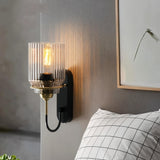 "A brass wall lamp with a ribbed glass shade in a bedroom with a pillow."