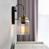 "A lit brass wall lamp with a ribbed glass shade on a light wall."