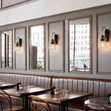 "Brass wall lamps with ribbed glass shades lining a restaurant wall with mirrors."