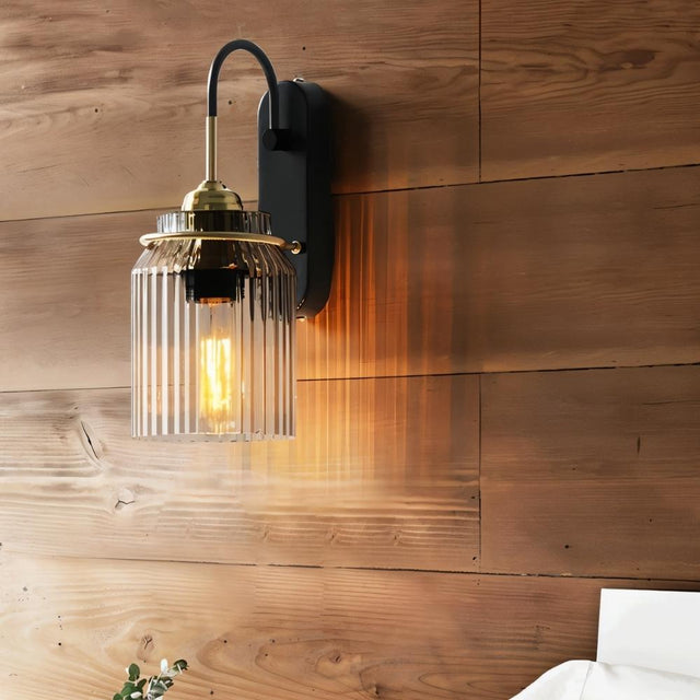 "A brass wall lamp with a ribbed glass shade on a wooden panel wall."