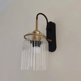 "A brass wall lamp with a ribbed glass shade on a light wall."