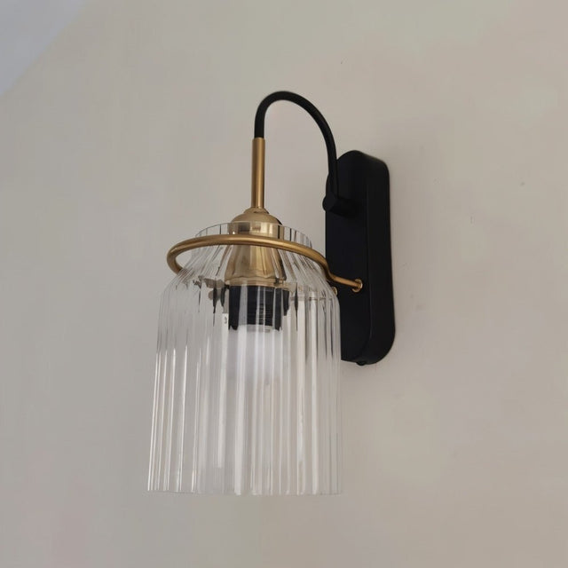 "A brass wall lamp with a ribbed glass shade on a light wall."