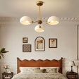 "A three-light chandelier with frosted glass shades hangs in a bedroom with a tufted headboard and framed artwork."