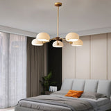 "A five-light chandelier with frosted glass shades hangs in a modern bedroom with a large window."