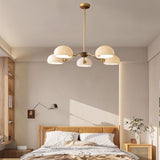"A modern chandelier with five dome-shaped glass shades hangs in a minimalist bedroom."