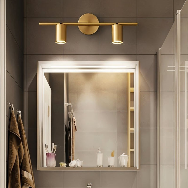 "A modern brass bathroom vanity light with two adjustable heads mounted on a circular base above a square mirror."