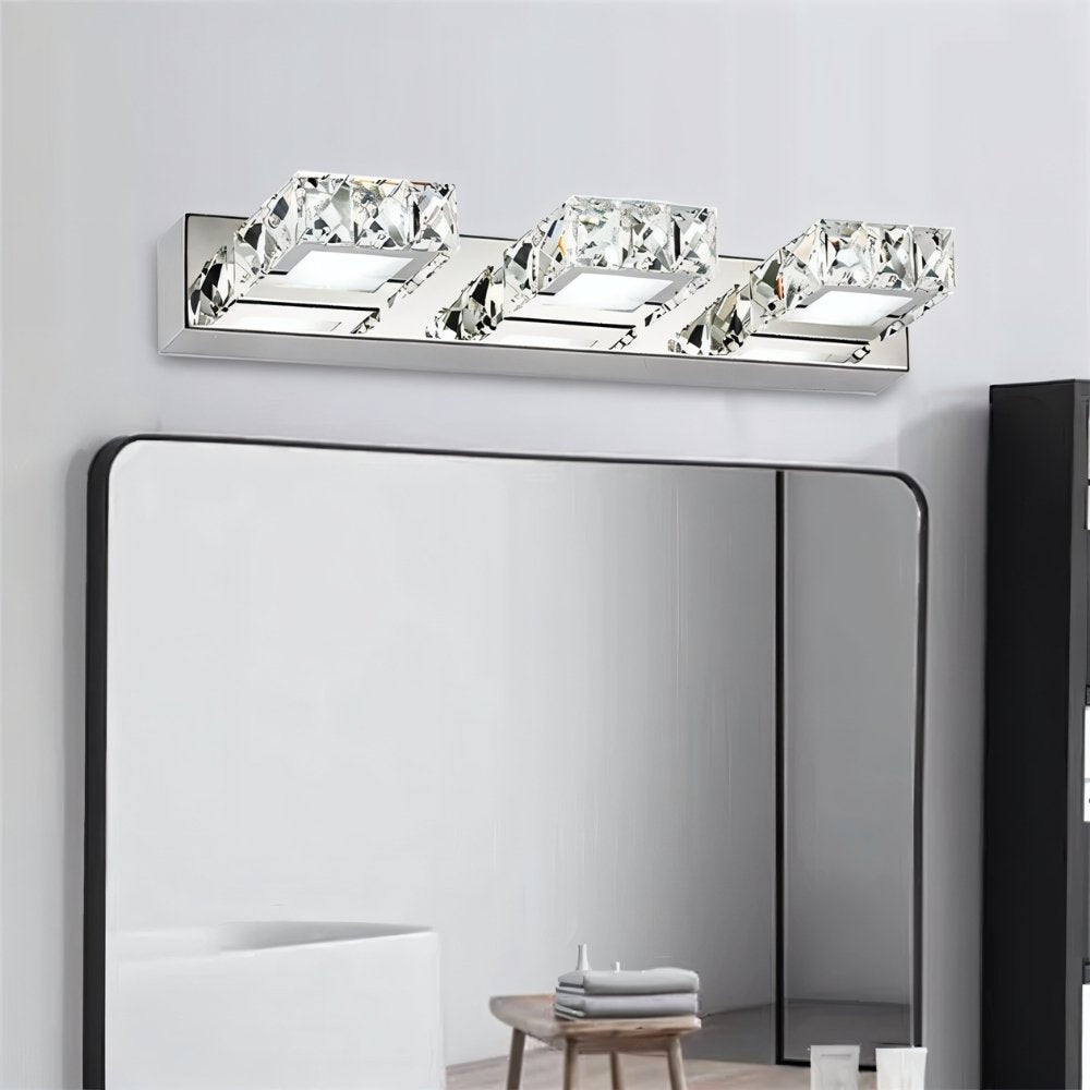 "A modern crystal and stainless steel bathroom vanity light mounted above a rectangular mirror in a contemporary bathroom."