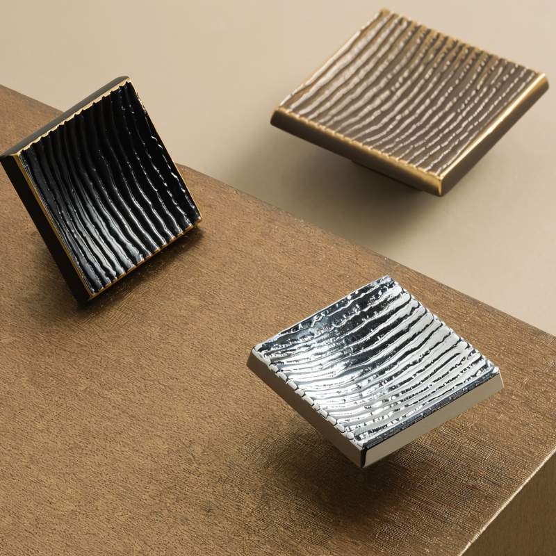 "Studio shot of modern square brass cabinet knobs with a textured, ridged surface in black, bronze, and silver finishes."
