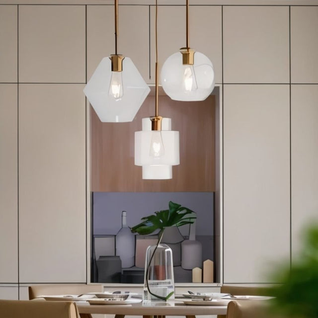 "Three clear glass pendant lights with different shapes hanging above a dining table."