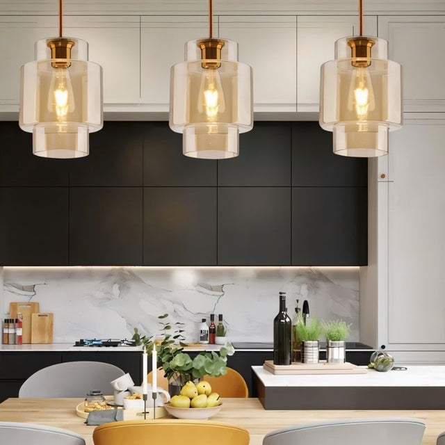 "Three amber glass cylindrical pendant lights hanging above a kitchen island."