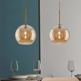 "Two amber glass sphere pendant lights hanging over a dining table with glasses."