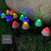 Solar-powered mushroom garden lights with multicolored LED tops illuminating grass and garden soil at dusk.
