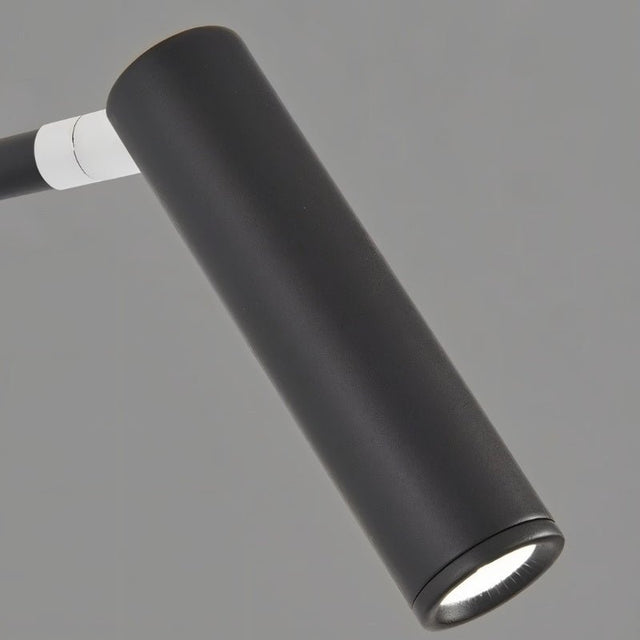 "A close-up of the lit cylindrical head of a black wall lamp with a pivoting arm."