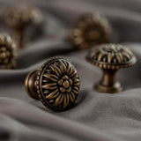 "Close-up of an antique brass floral knob with raised petal detailing on a gray fabric."