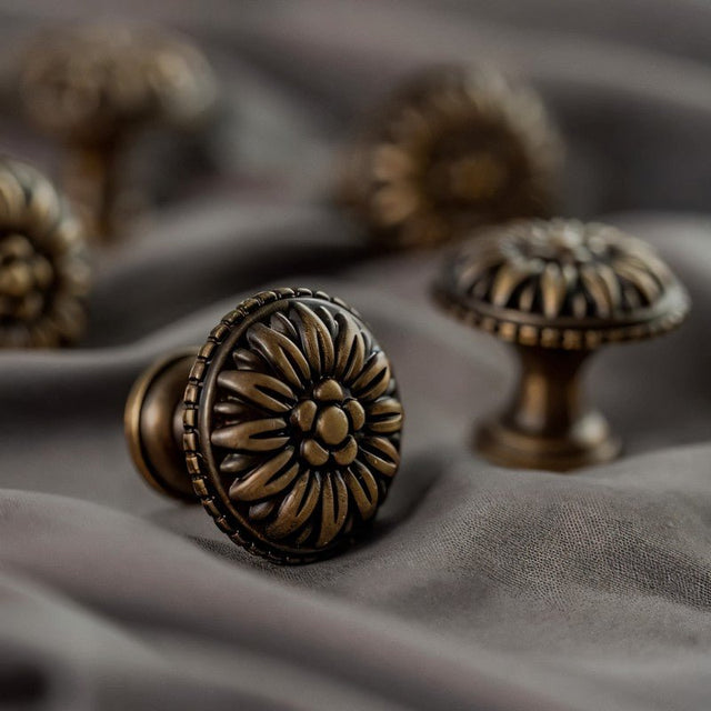 "Close-up of an antique brass floral knob with raised petal detailing on a gray fabric."