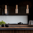 Nayra Copper Glass Pendant Light for Modern Spaces hanging above a dark kitchen island with minimalist decor and ribbed cabinetry.
