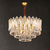 Round crystal chandelier with gold-finished brass frame and clear glass leaf-shaped crystals against dark background.